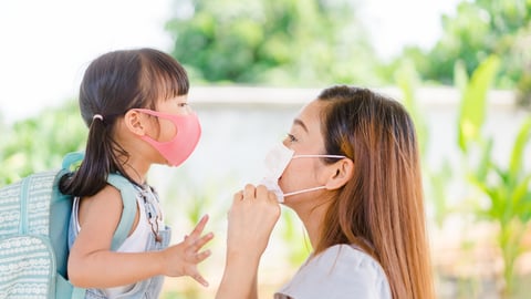 Mother dropping daughter off at school both wearing masks