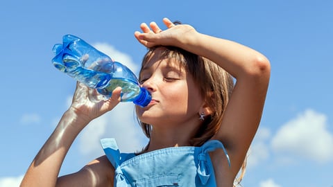 a young girl is drinking bottled water outside on a hot sunny day