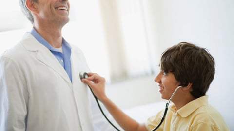 Young boy using  a stethoscope on a laughing doctor