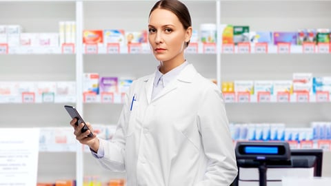 female pharmacist with serious expression holds her cellphone and looks at the camera