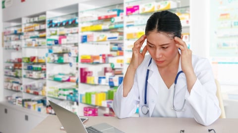 Pharmacist holding her head in her hands looking frustrated