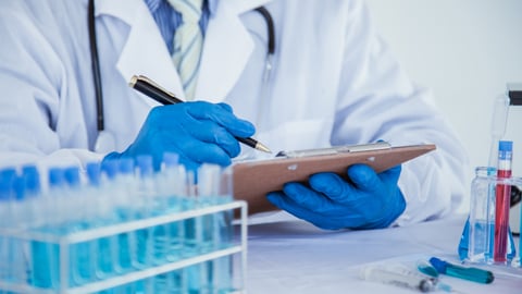 Close up a blue-gloved scientist noting results of an experiment