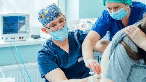 Two doctors giving a pregnant woman an epidural injection