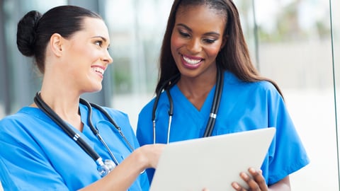 Two healthcare workers looking at a tablet and laughing