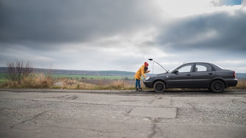 Woman looking under the hood of a car on the side of the road