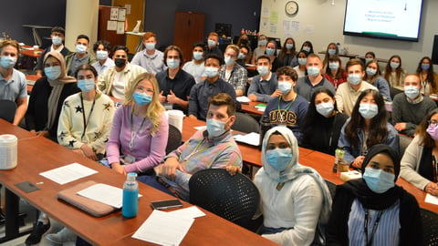 A group of medical students wearing masks in a classroom look at the camera.