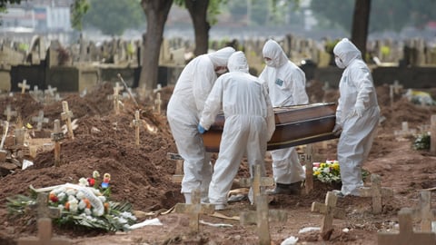 Four people wearing hazmat suits lowering a coffin