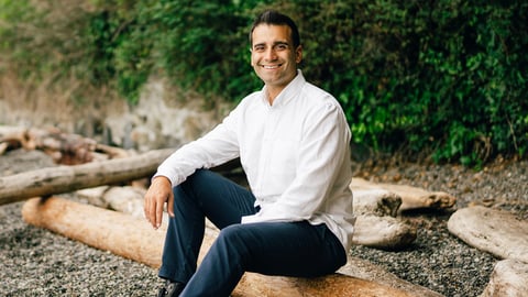 Man smiling in the white shirt and jeans sitting on a log