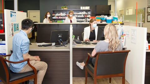 Two pharmacy customers sitting across from technicians