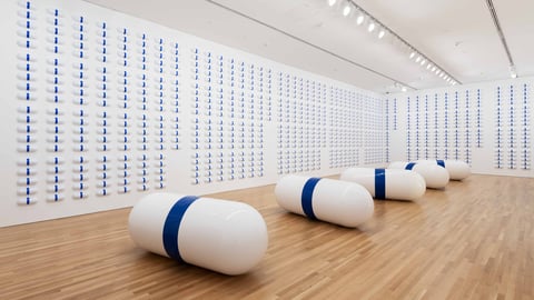 A white room with giant blue and white pills lining the walls and on the floor.