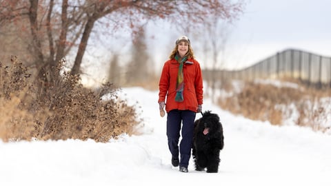 Woman wearing a red coat walker her dog in the snow