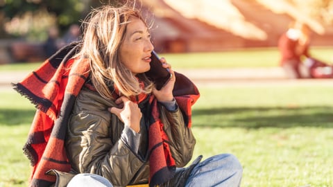 A woman sitting on grass with blanket on her shoulders