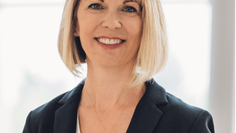 A headshot of a white woman with blond hair wearing a dark suit jacket