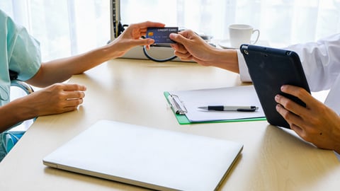 Close up of desk and patient hand reaching over to doctor's hand to pay with credit card 