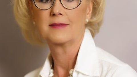 A blond woman in a white collared shirt wearing glasses