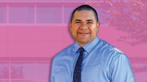 Man in blue shirt standing in front of pink background