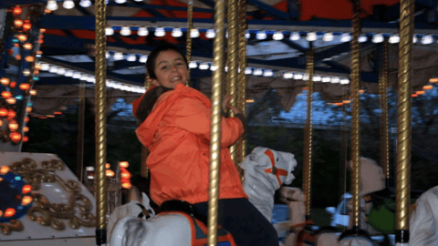 A boy in red jacket, smiling as he rides a merry go round hore