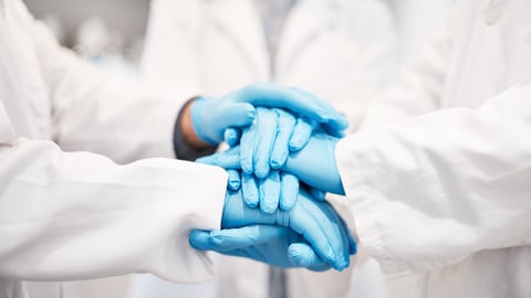 Doctors with white coats and blue gloves putting their hands together