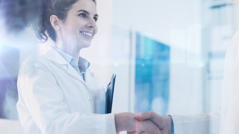 Young woman doctor with a pony tail and white coat shaking the hand of a person out of frame