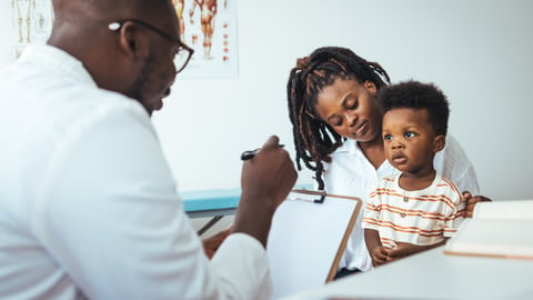 Black male doctor talking to a young Black toddler sitting on her mother's lap