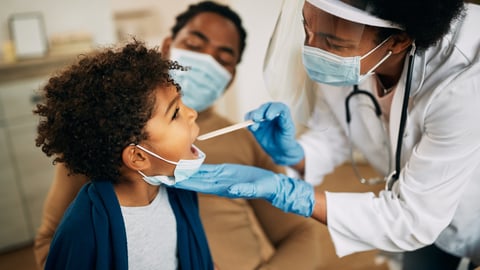 Black woman doctor wearing mask and face shield examining a Black toddler