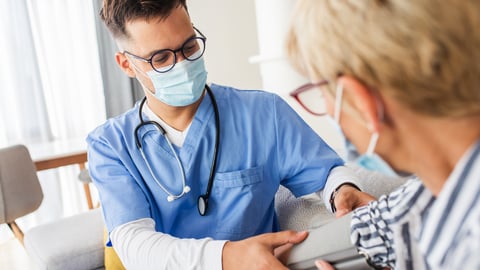 Male nurse with blue scrubs and a mask talking with an older female patient