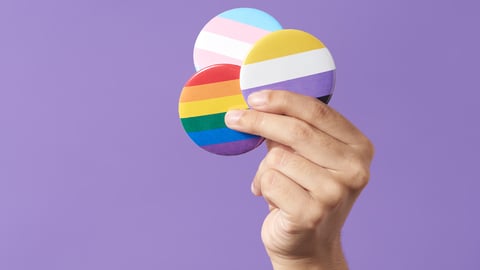 White hand holding up buttons denoting different pride flags