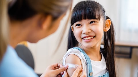 Young girl smiling as a physician puts a bandaid over her vaccination jab