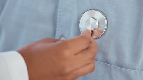 Brown hand of a doctor pressing a stethoscope to a patient's chest