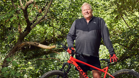 Older white man standing in the woods with a red bike