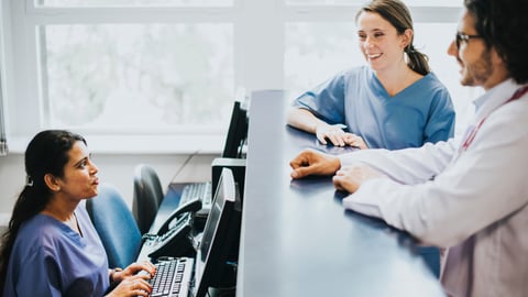 female medical receptionist at desk talking to two female colleagues