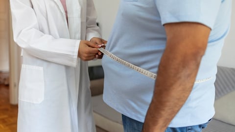 doctor in white coat measures waist of large man with measuring tape