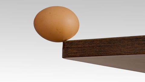 An egg balanced on the edge of a ledge