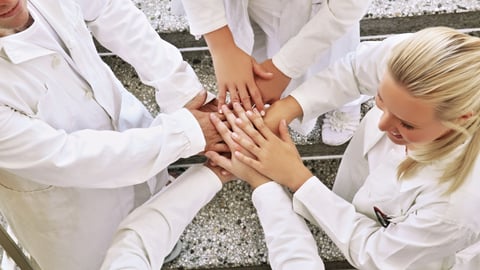 Healthcare workers in a circle with their hands together in the middle