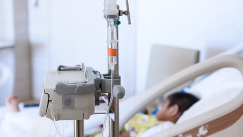 A young child in a hospital bed with an IV in the foreground