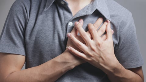 chest of young white man, gray shirt, holding left side of his chest