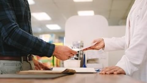 Torsos of patient handing prescription paper to pharmacist