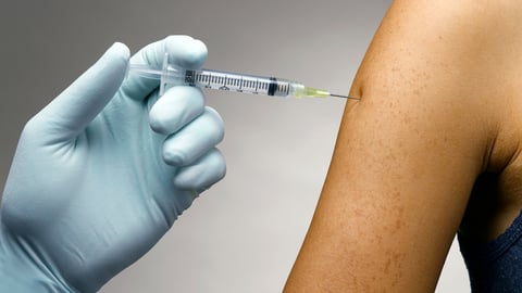 Blue gloved hand giving a vaccine into a waiting arm