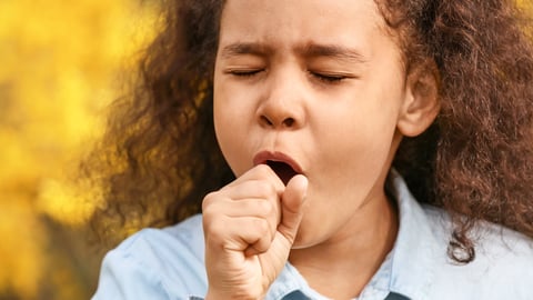 Young Black girl coughing into her hand