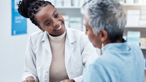 Black female pharmacist smiling with black older woman patient