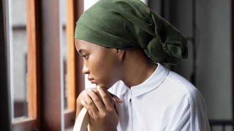 Black woman wearing green scarf on head suggesting hair loss, looking sad