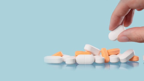 opioid pills or other pills on blue background, white hand selecting a pill