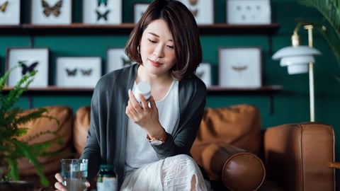 A young Asian woman in a well-decorated room looking contemplatively at the pill bottle