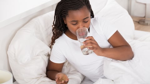 Young Black girl in bed taking a pill with a tall glass of water