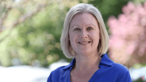 Pharmacist Tracey Thornley, a fair-skinned woman with blonde hair smiling for a photo with flowering trees in the background