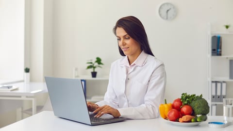 Young healthcare professional at laptop at kitchen table