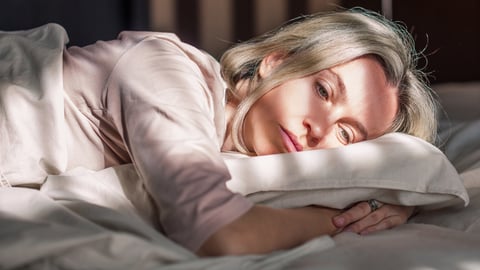 Stressed middle aged woman lying on bed at home and crying.