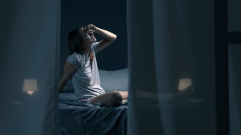 Woman on bed at night, stressed, hand on head, tired or hot, can't sleep