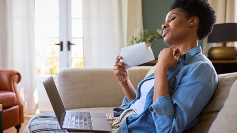 Middle-aged black woman sitting with a lap top, too hot too work, fanning herself