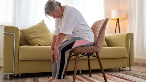 Older white woman doing chair yoga in her living room